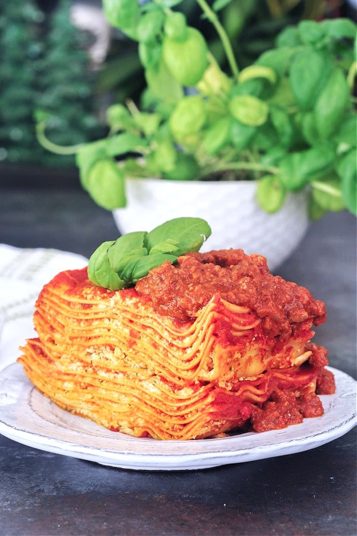 Twelve layer slice of gluten free Vegan Lasagna on a rustic plate, garnished with fresh basil.