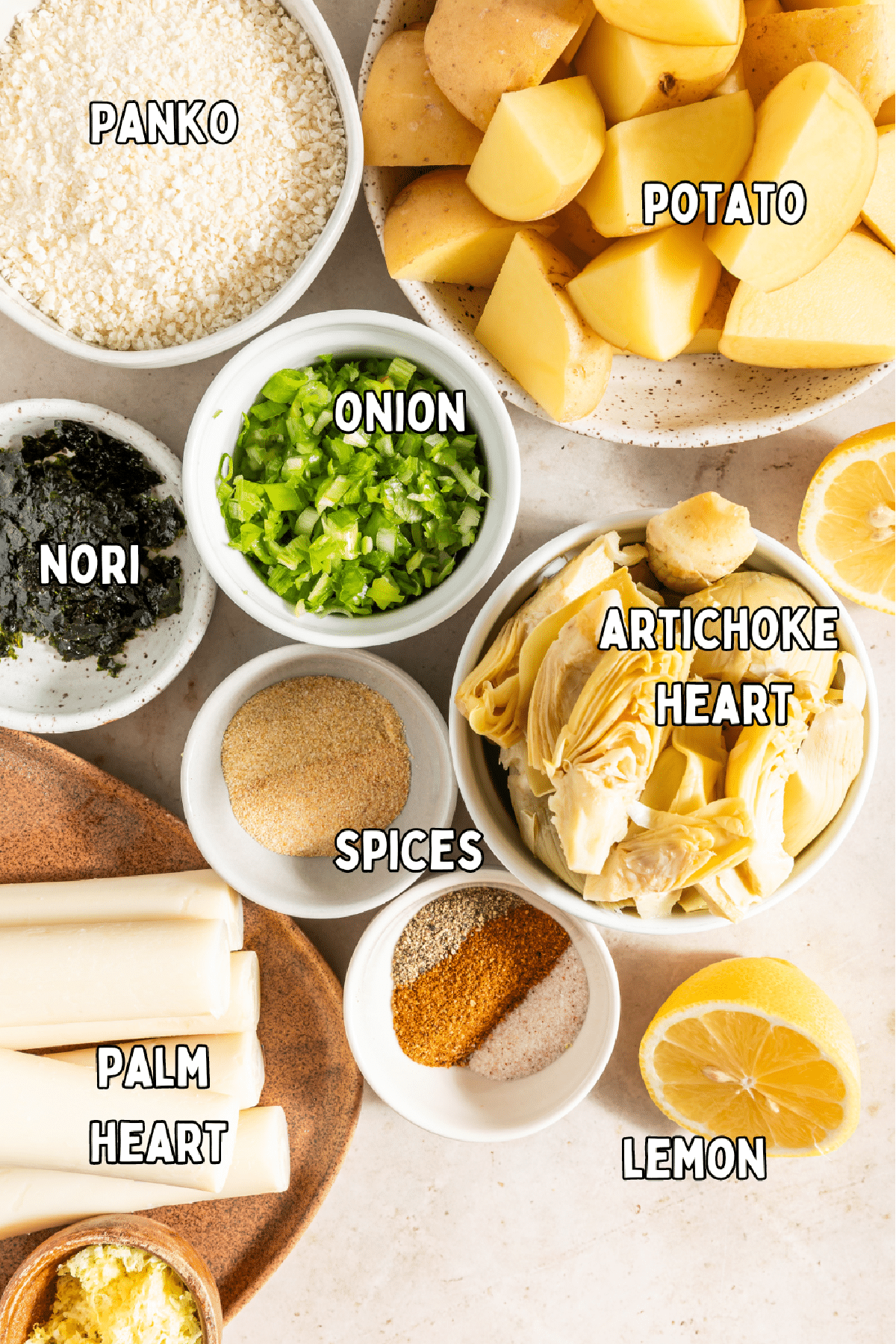 Overhead view of vegan crab cake ingredients: panko, potatoes, onion, nori, artichoke hearts, spices, palm hearts, and lemon.