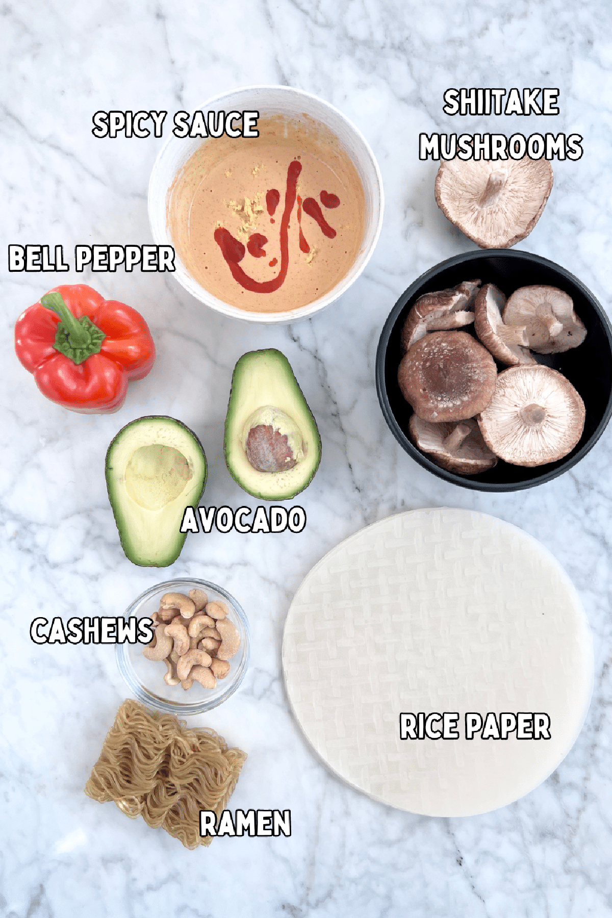 Overhead view of ingredients for avocado shiitake spring rolls: spicy sauce, shiitake mushrooms, bell pepper, avocado, cashews, ramen noodles, round rice paper wrappers.