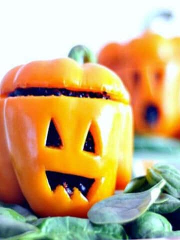 Two orange bell peppers carved into jack o lanterns and stuffed with a ginger carrot quinoa filling.