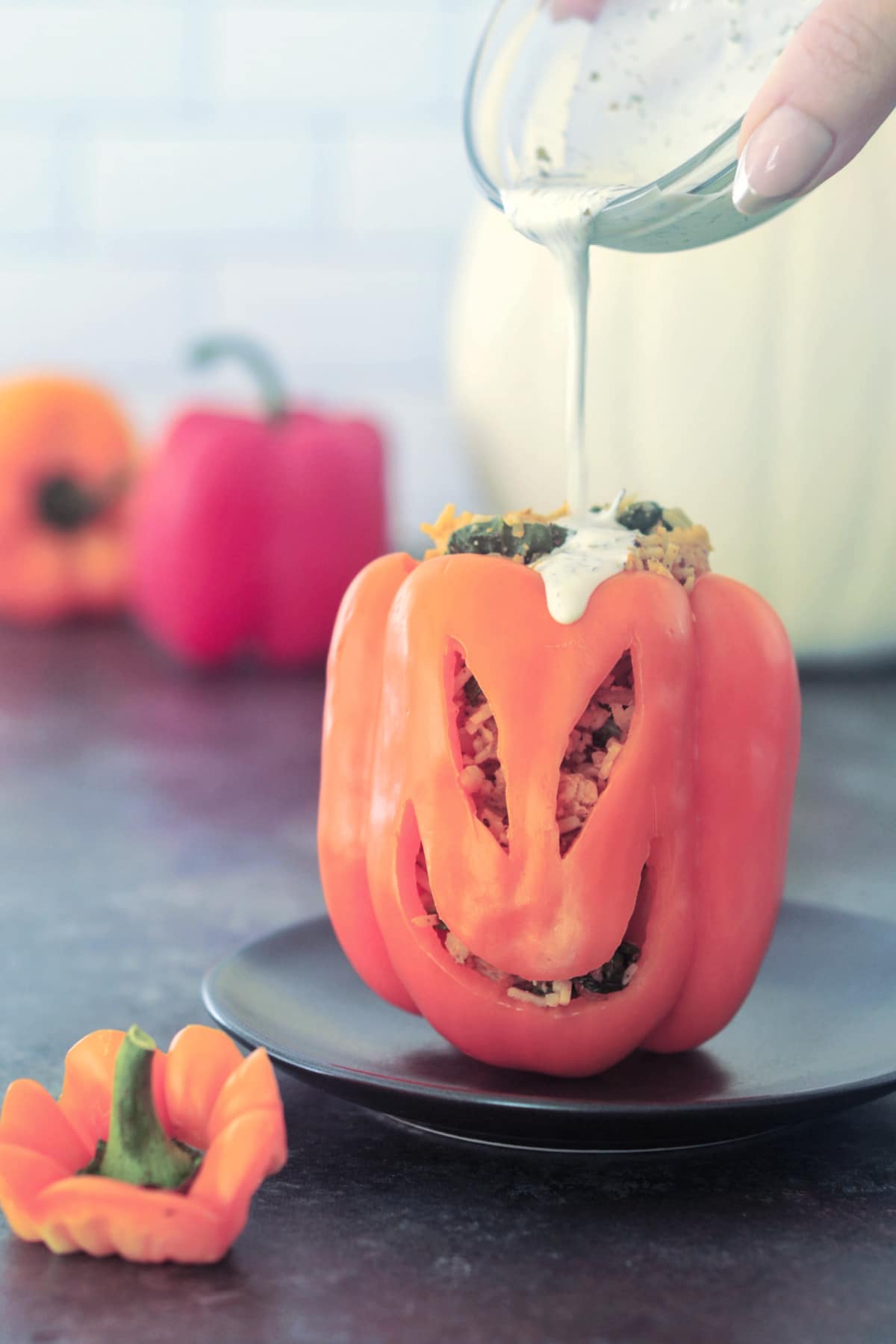 An orange bell pepper carved with a Halloween jack o lantern face, then filled with vegan buffalo chicken, rice, and veggies. A hand is pouring ranch dressing onto the top of the bell pepper.