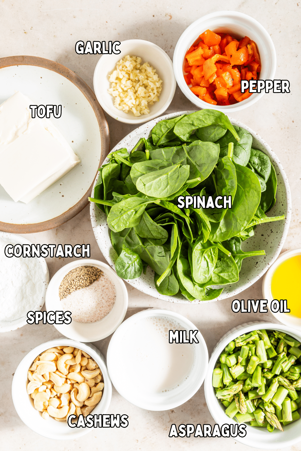 Bowls of ingredients to make vegan egg bites: tofu, garlic, pepper, spinach, cornstarch and spices, milk, cashews, asparagus and olive oil.