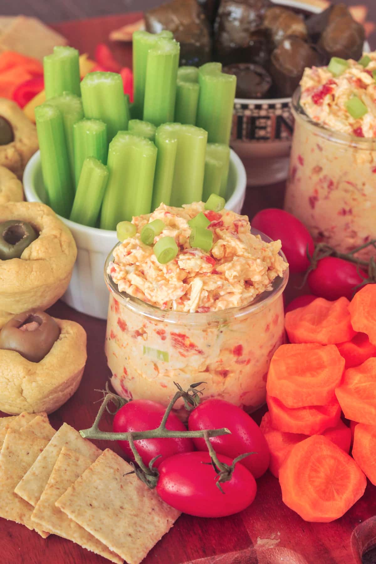 Pimiento cheese in a small glass jar, surrounded by veggies and crackers on a snack board.