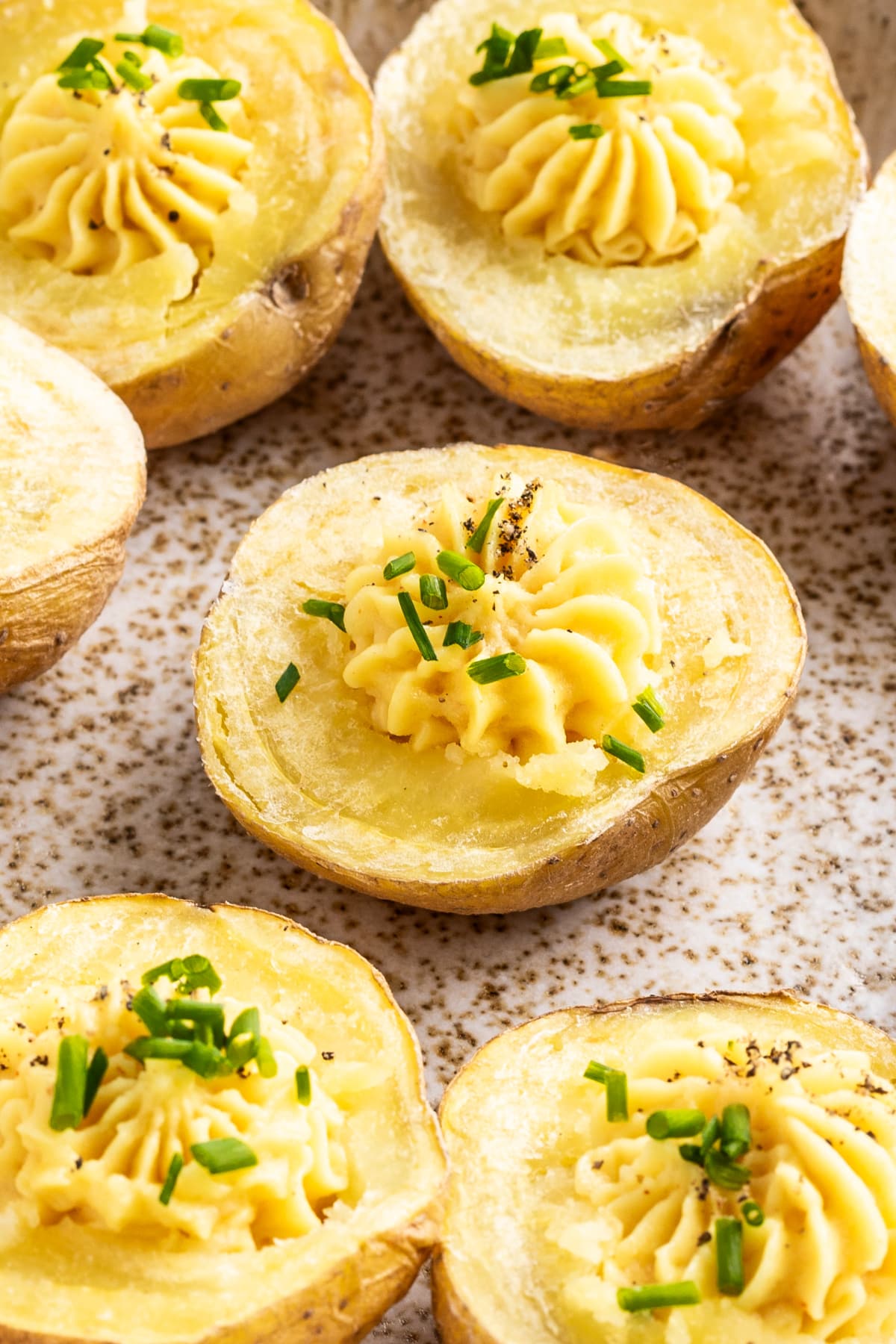 Close up of mini gold potatoes sliced in half, baked, scooped out and filled with a deviled egg flavored mixture. These deviled potatoes are sitting on a tan speckled dish for serving.