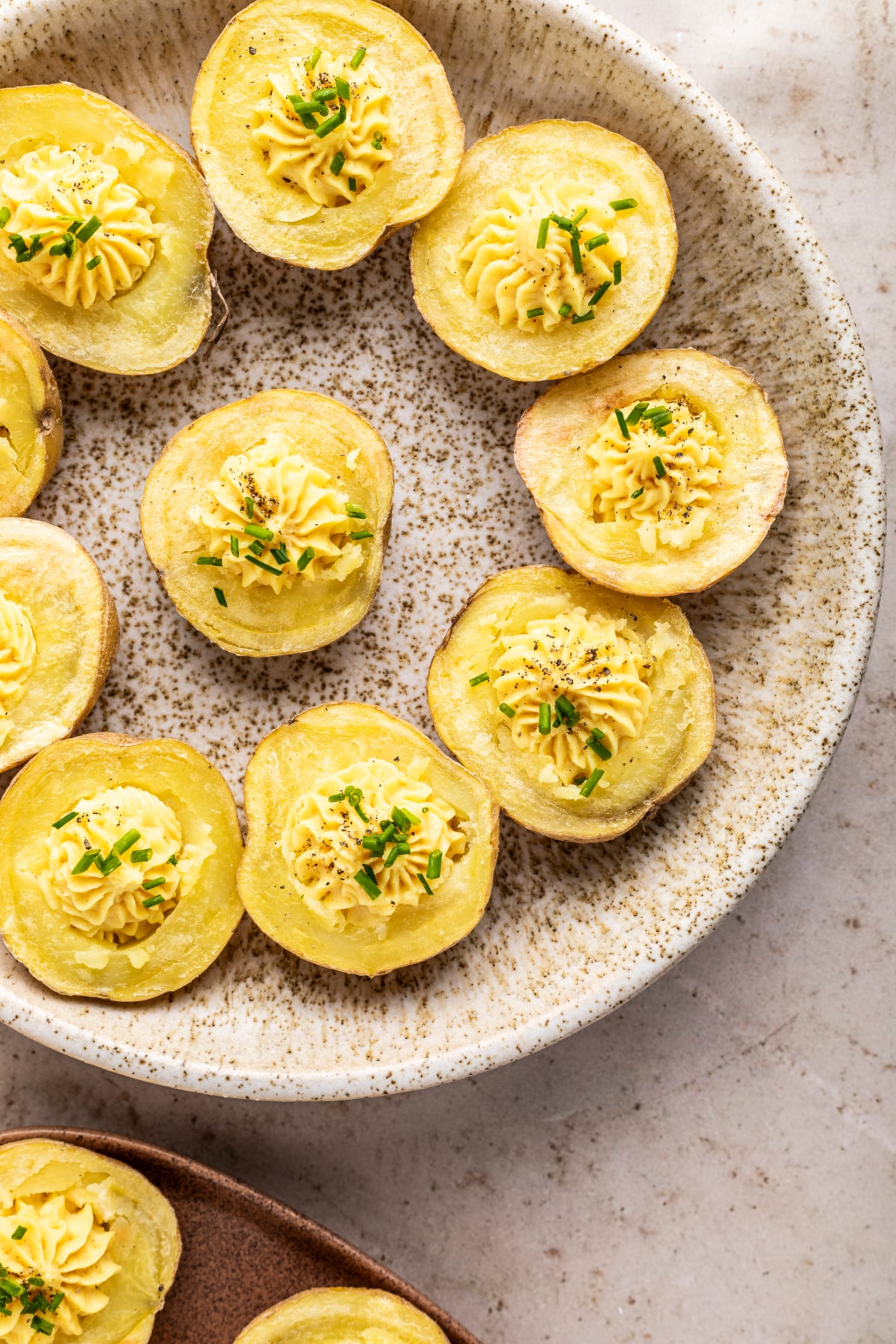Overhead view of mini gold potatoes sliced in half, baked, scooped out and filled with a deviled egg flavored mixture. These deviled potatoes are sitting on a tan speckled dish for serving.