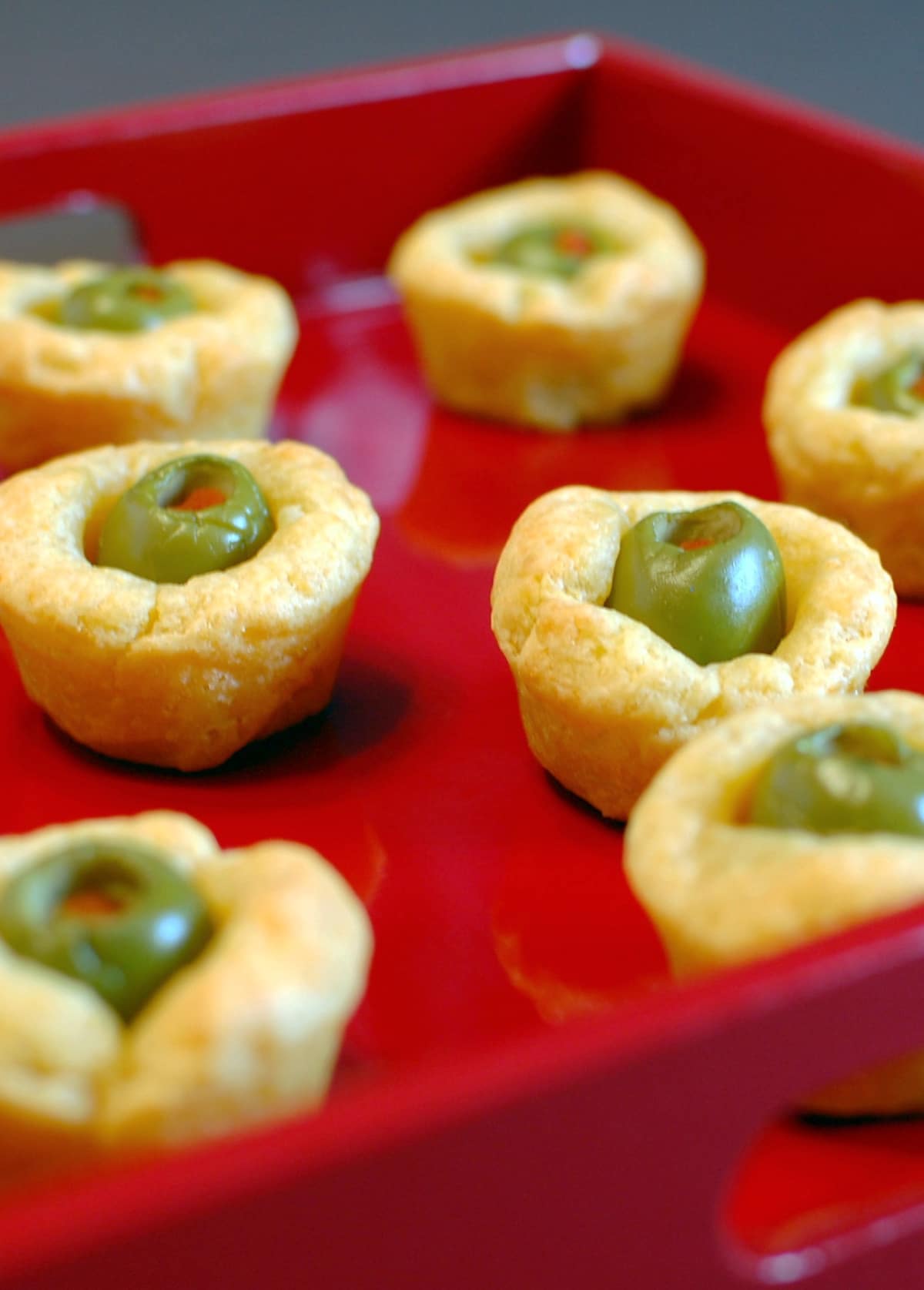 Pimiento stuffed olives wrapped in cheese dough served on a bright red tray.
