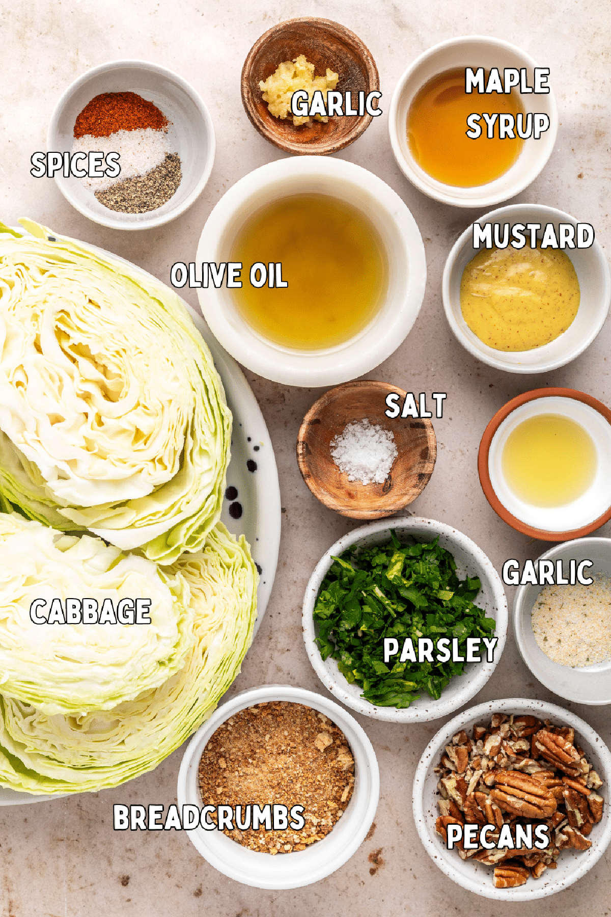 Overhead view of ingredients for cabbage steaks: cabbage, spices, olive oil, garlic, maple syrup, mustard, parsley, breadcrumbs, pecans.