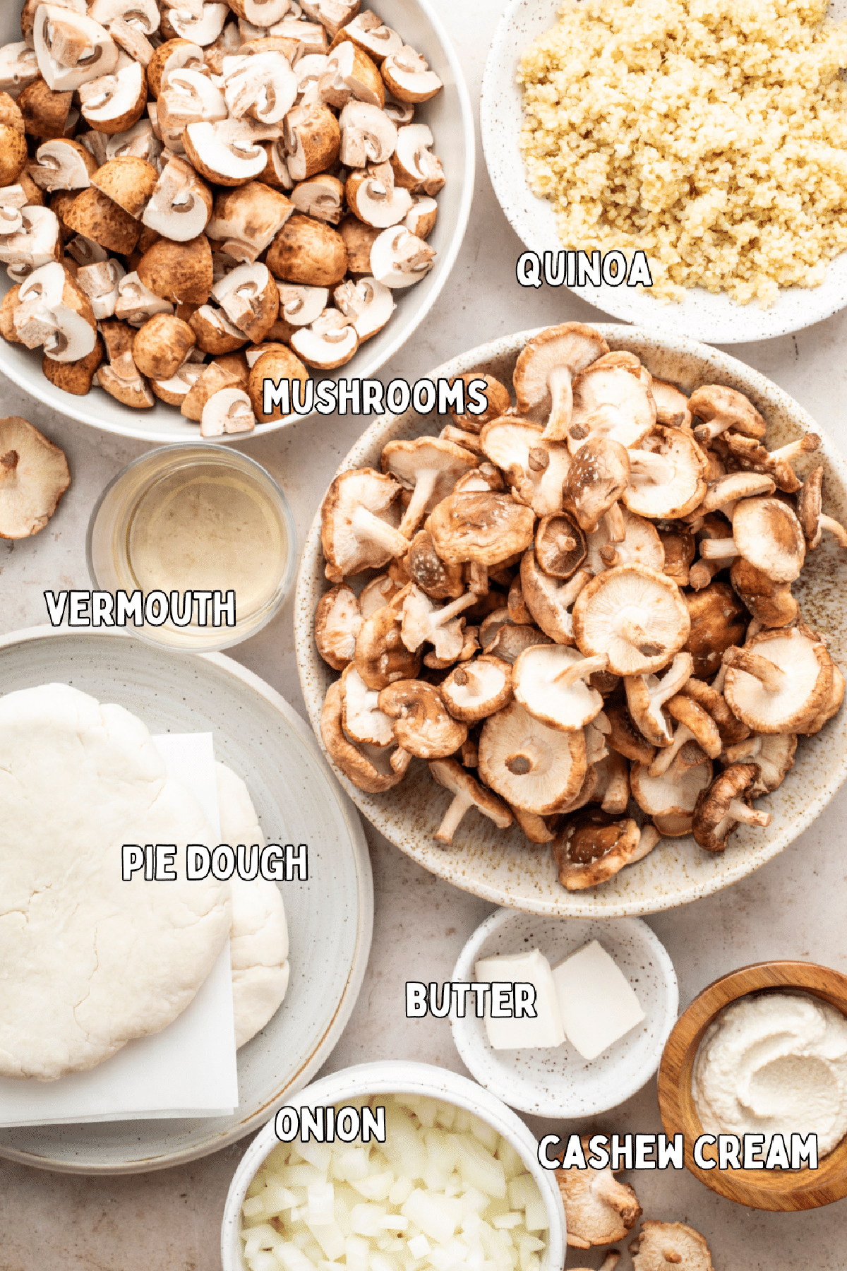 Overhead view of various bowls of ingredients to make a mushroom quinoa pie: two kinds of mushrooms, cooked quinoa, vermouth, pie dough, butter, cashew cream, and onions.
