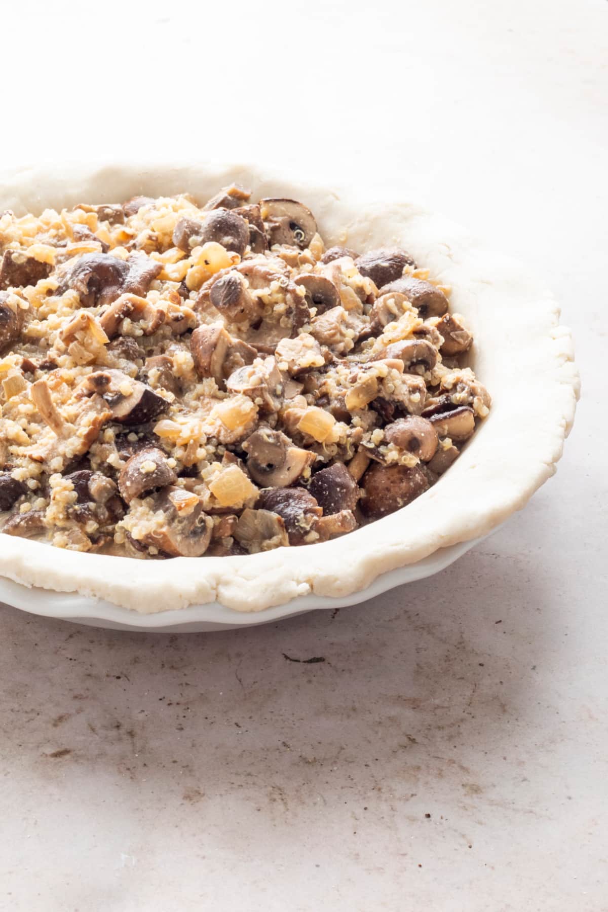 A pie plate lined with a bottom crust and filled with a savory mushroom quinoa filling.