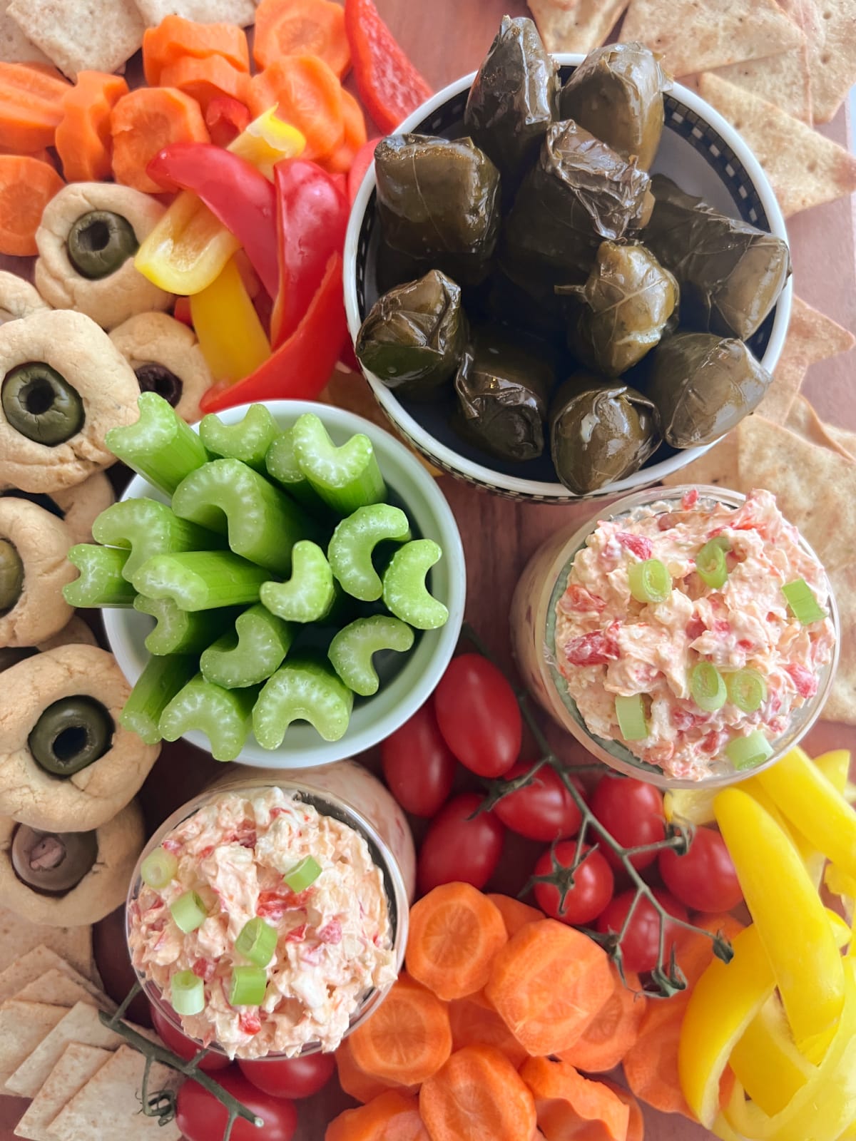 Overhead view of pimiento cheese in two small glass jars, surrounded by veggies and crackers on a snack board.