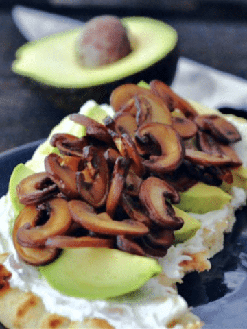 A slice of flatbread topped with vegan goat cheese, avocado slices, and sautéed mushrooms.