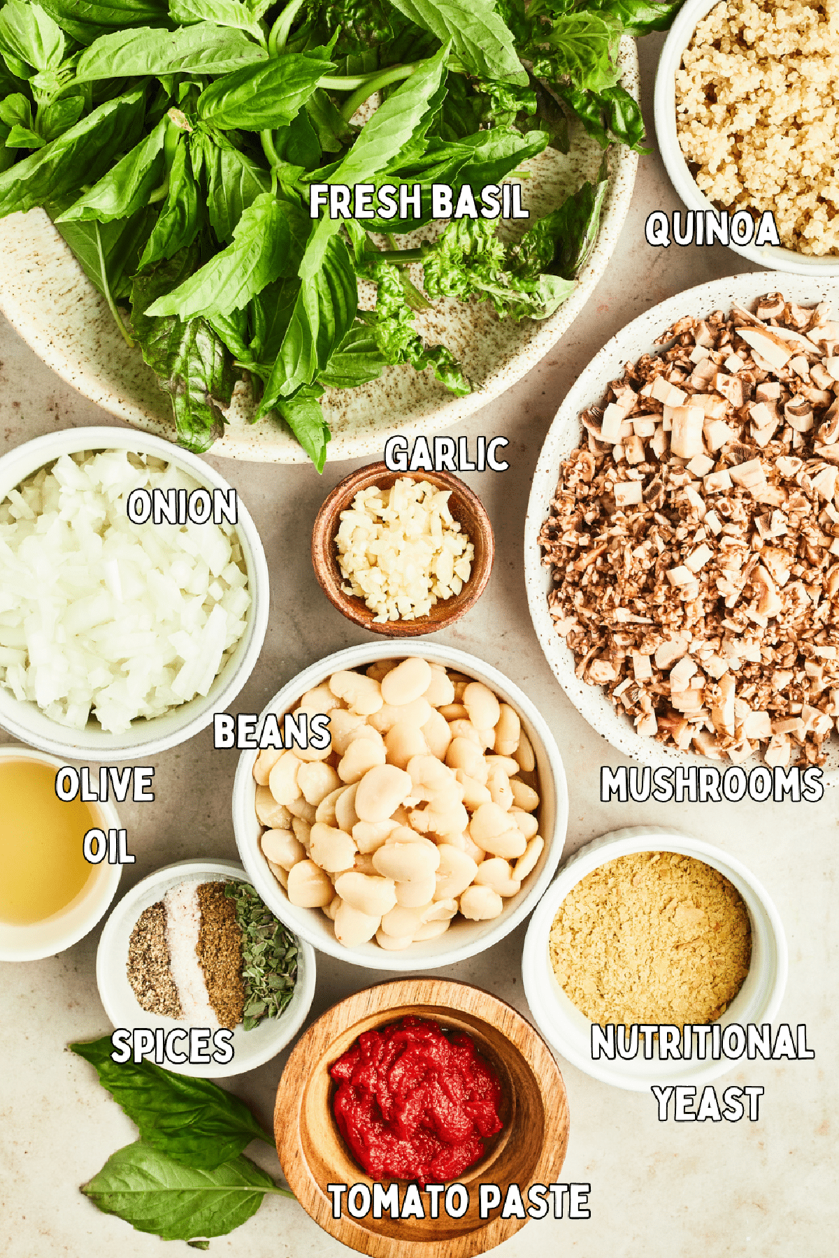 Overhead view of several bowls of ingredients to make basil quinoa meatballs: fresh basil, quinoa, mushrooms, garlic, onion, beans, nutritional yeast, tomato paste, olive oil, and spices.