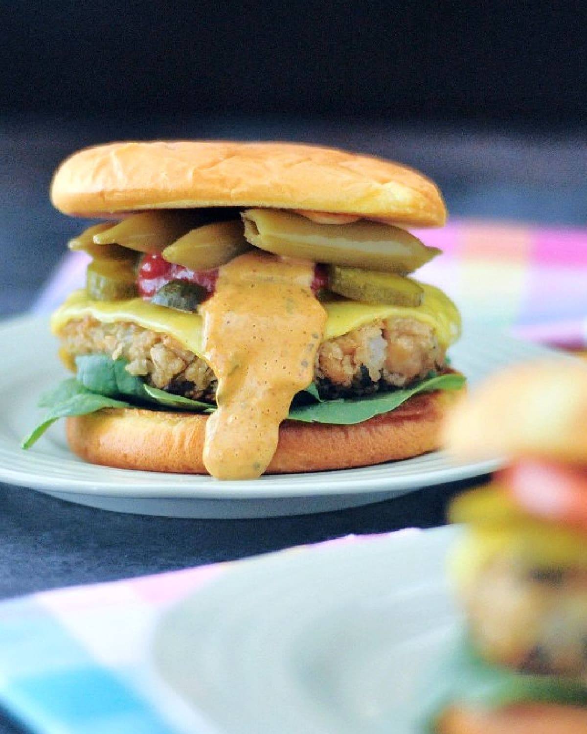 Side view of a veggie burger dressed with fresh spinach, a slice of melting cheese, chipotle ranch dressing, and pickled veggies.