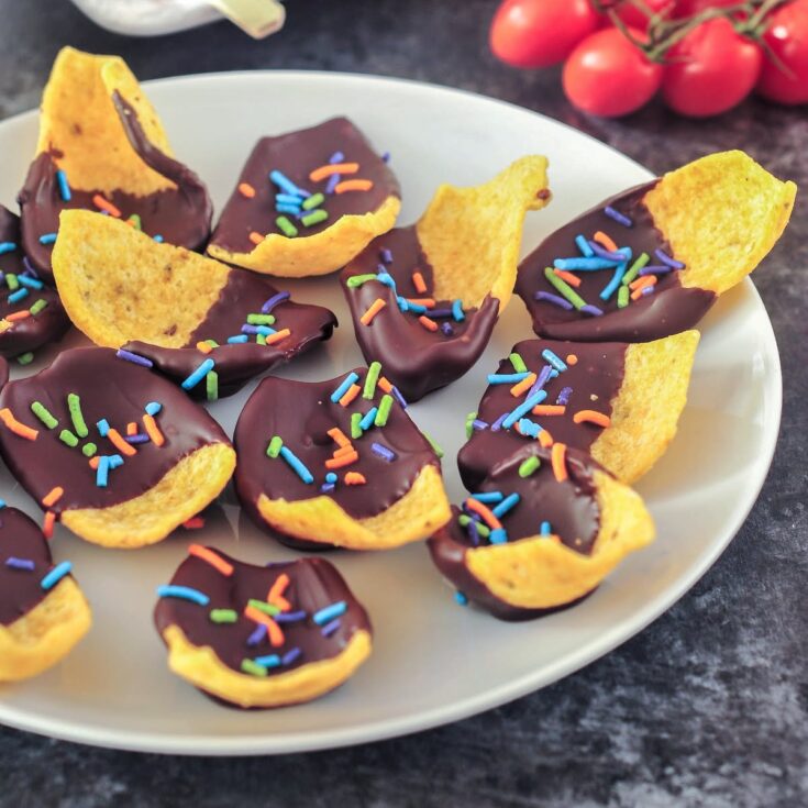 A white plate of chocolate dipped corn chips with multi colored sprinkles in the chocolate.