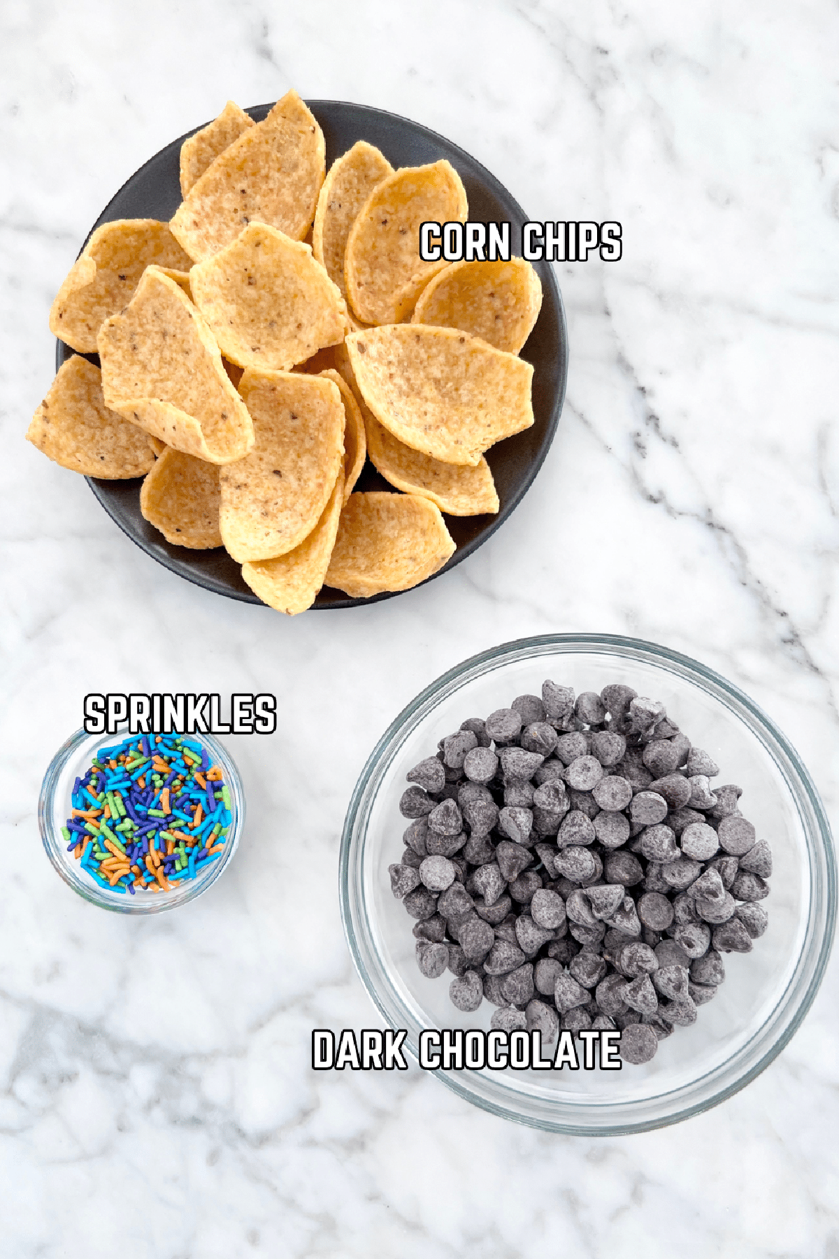 Three bowls of ingredients to make chocolate dipped corn chips: chips, dark chocolate, and colorful sprinkles.