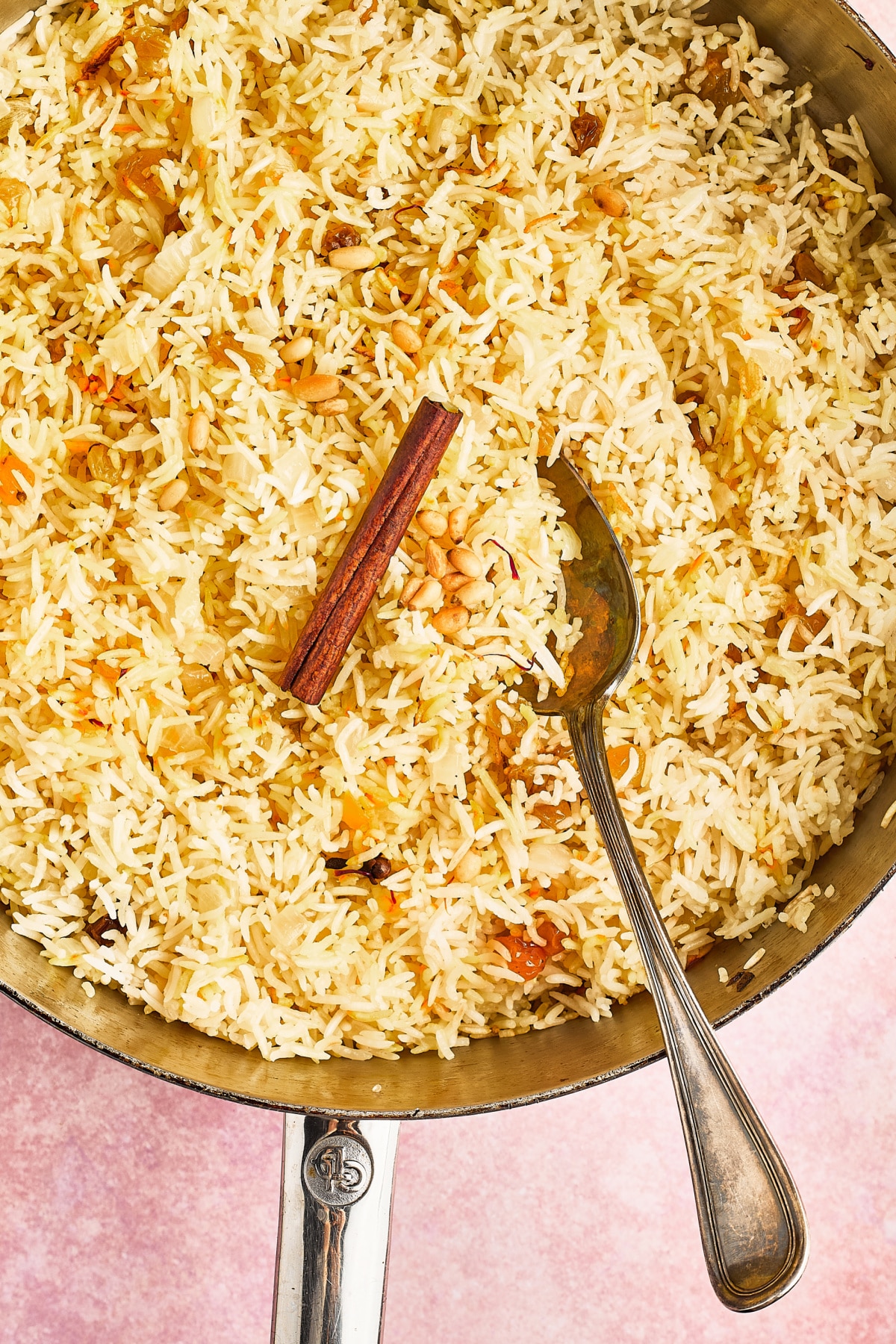Overhead view of a skillet of yellow saffron rice garnished with golden raisins, pine nuts, a cinnamon stick and saffron strands.