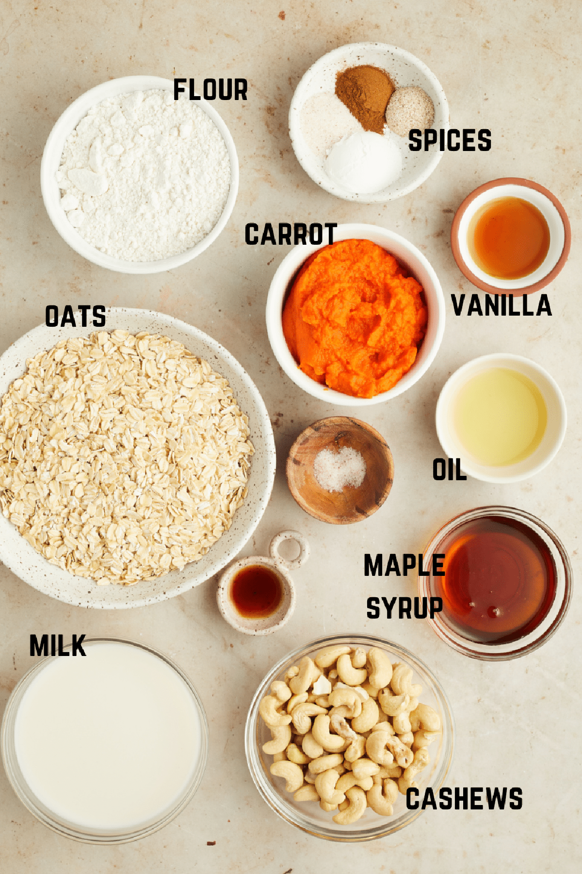 Overhead view of ingredients to make carrot pancakes: flour, oats, carrot, spices, vanilla, oil, maple syrup, cashews, and milk.