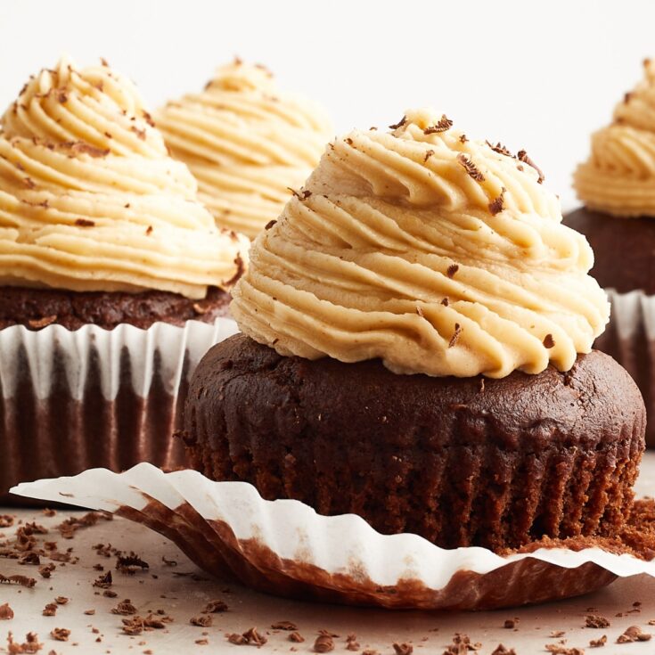 Several chocolate cupcakes with peanut butter frosting piped on top. The cupcake in front has the white paper wrapper partially removed.