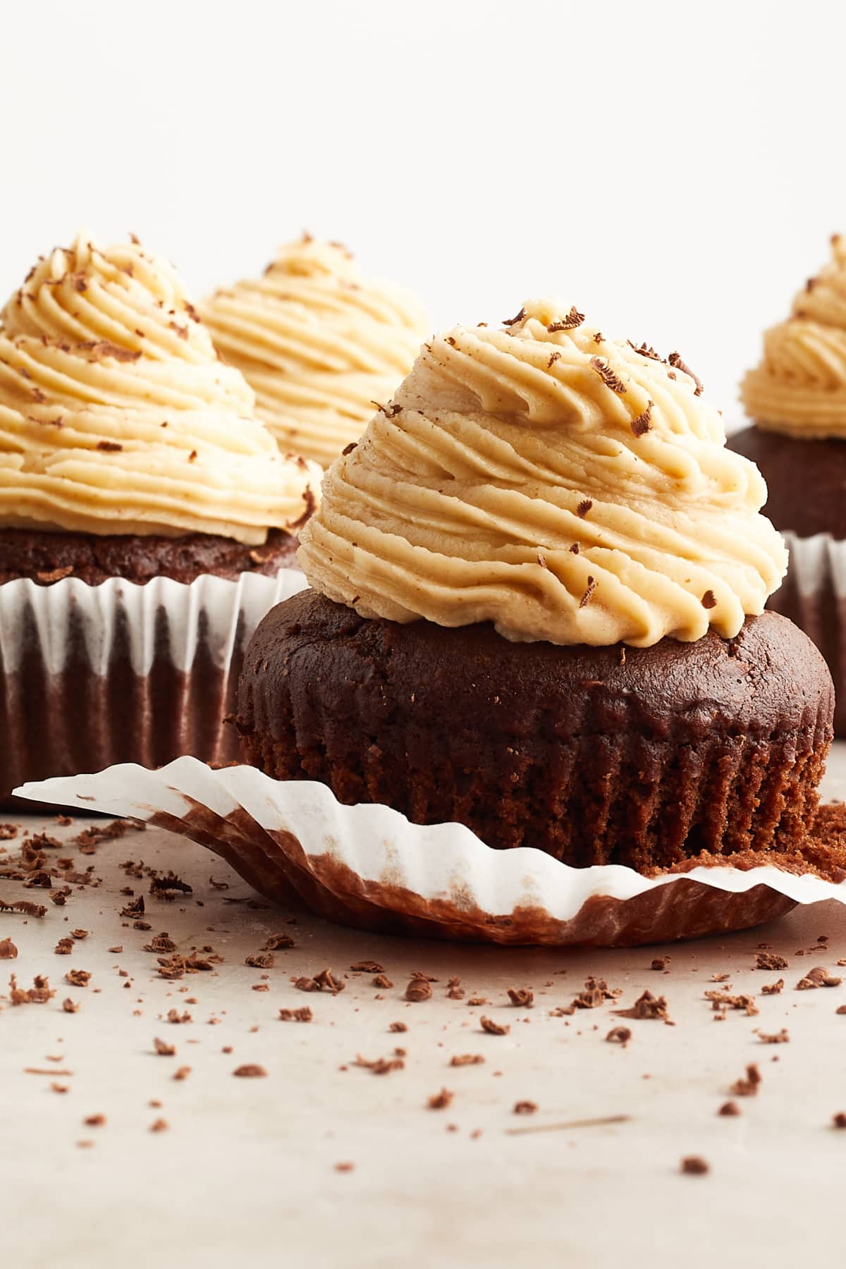 Several chocolate cupcakes with peanut butter frosting piped on top. The cupcake in front has the white paper wrapper partially removed.