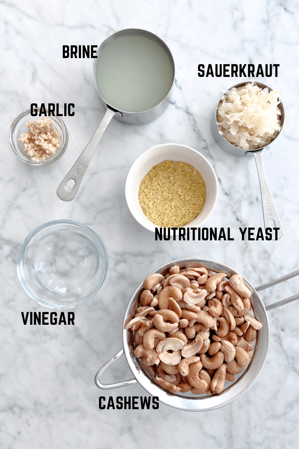 Overhead view of ingredients for vegan cheese sauce: sauerkraut and brine, garlic, nutritional yeast, vinegar, and cashews.
