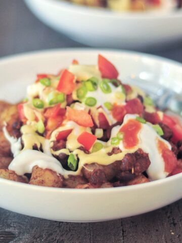 A shallow bowl filled of black bean totchos topped with garlic lemon sauce, tomatoes, jalapeños, salsa, and green onions.