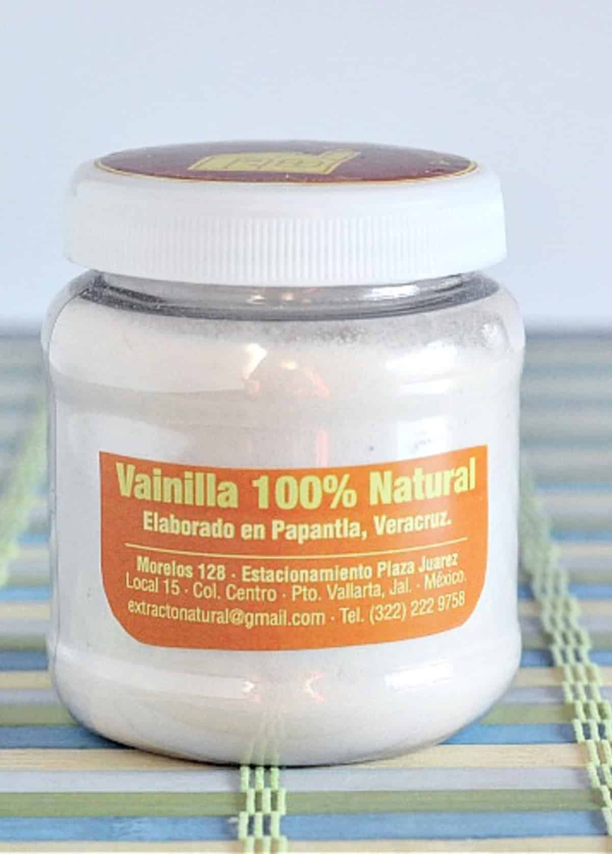 A jar of vanilla powder sits on a blue and green striped mat.