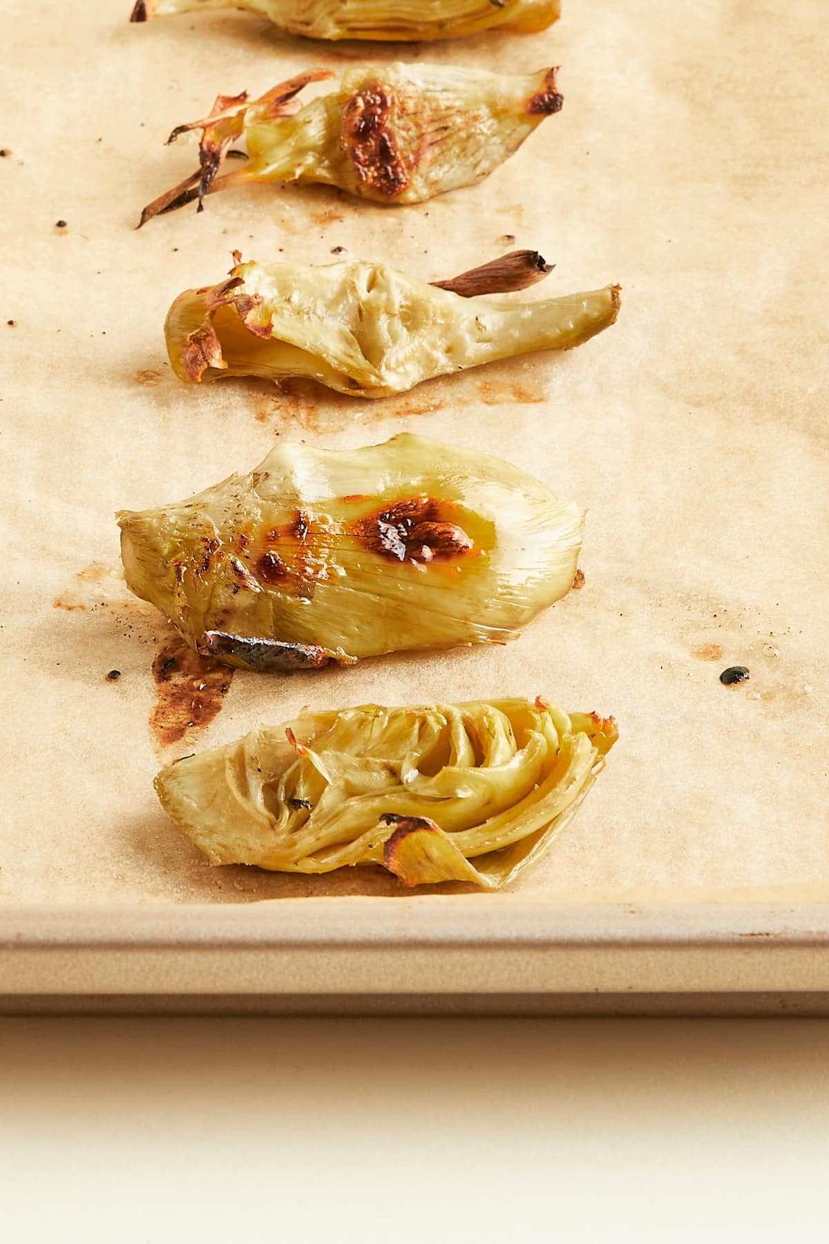 Roasted artichoke hearts lined up in a row on a parchment lined baking sheet.
