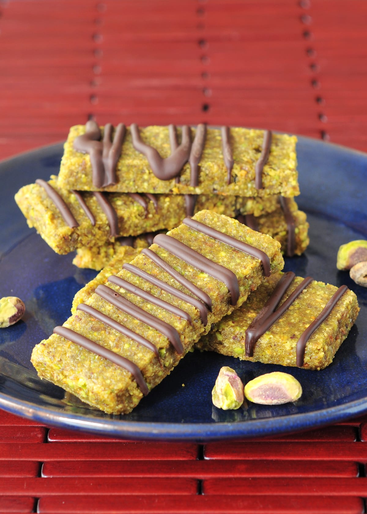 Light green pistachio bars drizzled with chocolate are stacked on a navy blue plate.