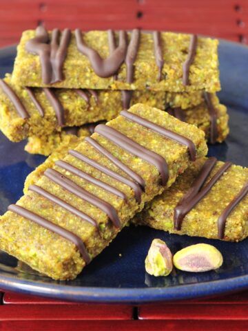 Light green pistachio lime bars drizzled with chocolate are stacked on a navy blue plate.