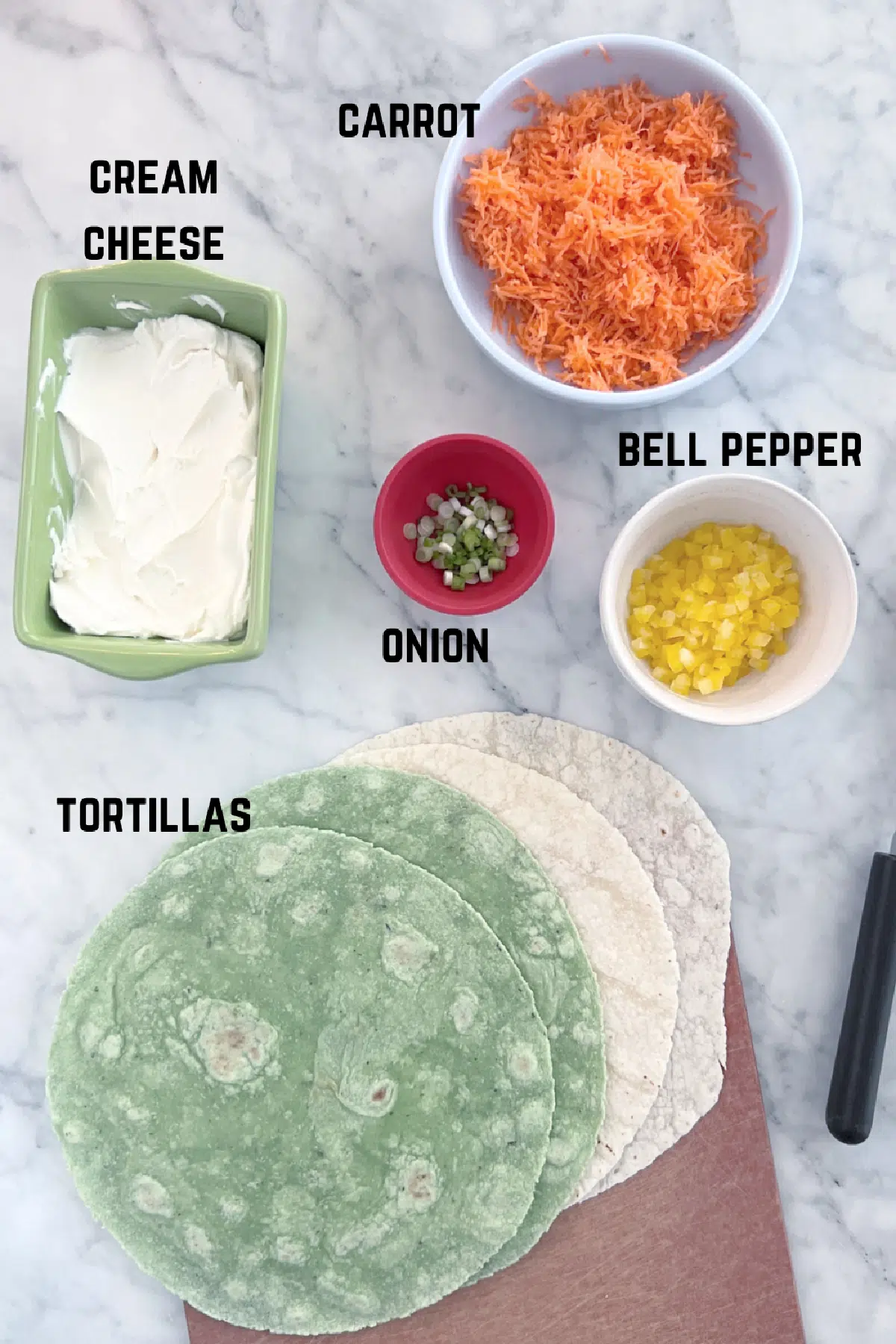 Overhead view of ingredients to make veggie pinwheels: grated carrot, cream cheese, green onion, bell pepper, tortillas.