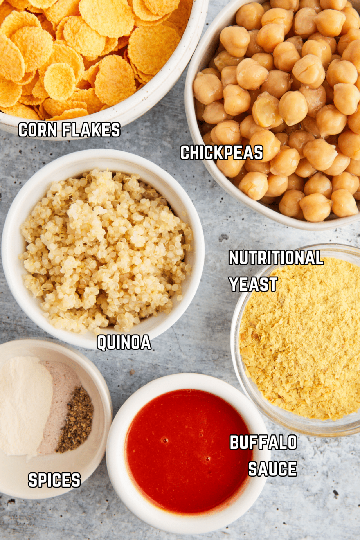 Overhead view of bowls of ingredients to make vegan wings: cornflakes, chickpeas, quinoa, nutritional yeast, buffalo sauce, and spices.