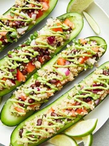 Overhead view of a plate of cucumber boats filled with a tex mex mixture of beans, quinoa, tomato and onion, and drizzled with a tangy avocado sauce.