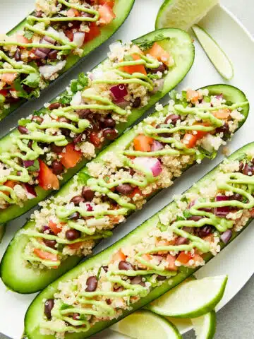 Overhead view of a plate of cucumber boats filled with a tex mex mixture of beans, quinoa, tomato and onion, and drizzled with a tangy avocado sauce.