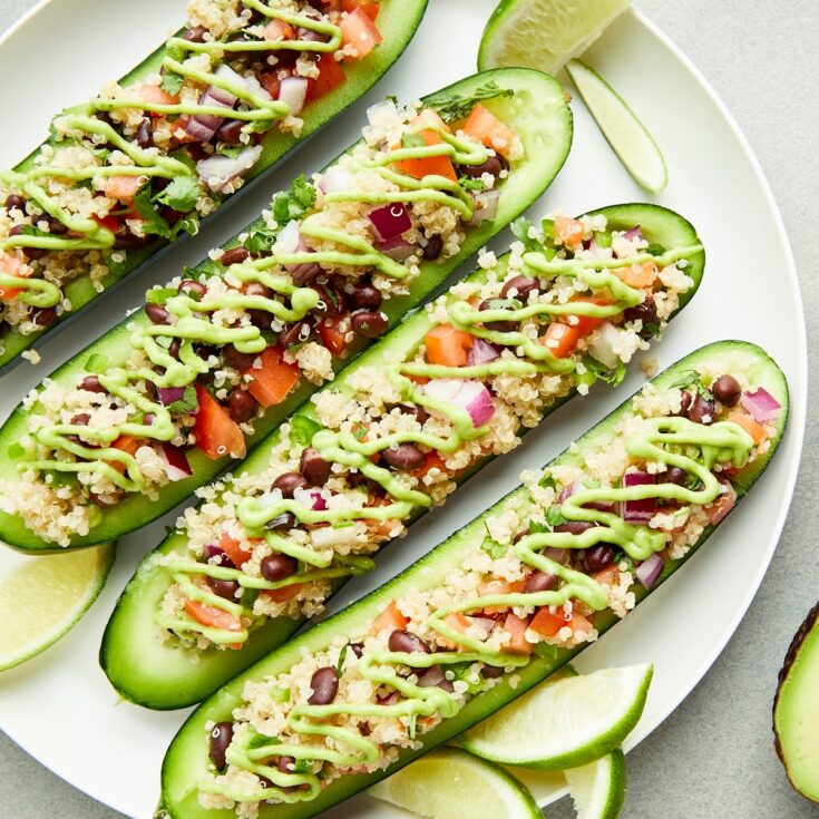 Overhead view of a plate of cucumber boats filled with a tex mex mixture of beans, quinoa, tomato and onion, and drizzled with a tangy avocado sauce.