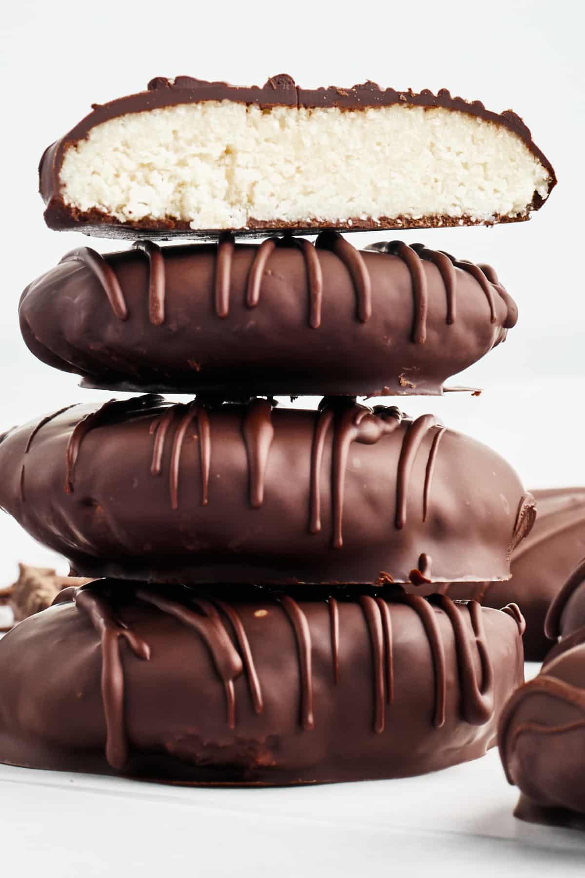 Side view of a stack of 4 peppermint patties on a white surface, with more sitting next to the stack. The top one on the stack is sliced open to see the bright white peppermint filling.