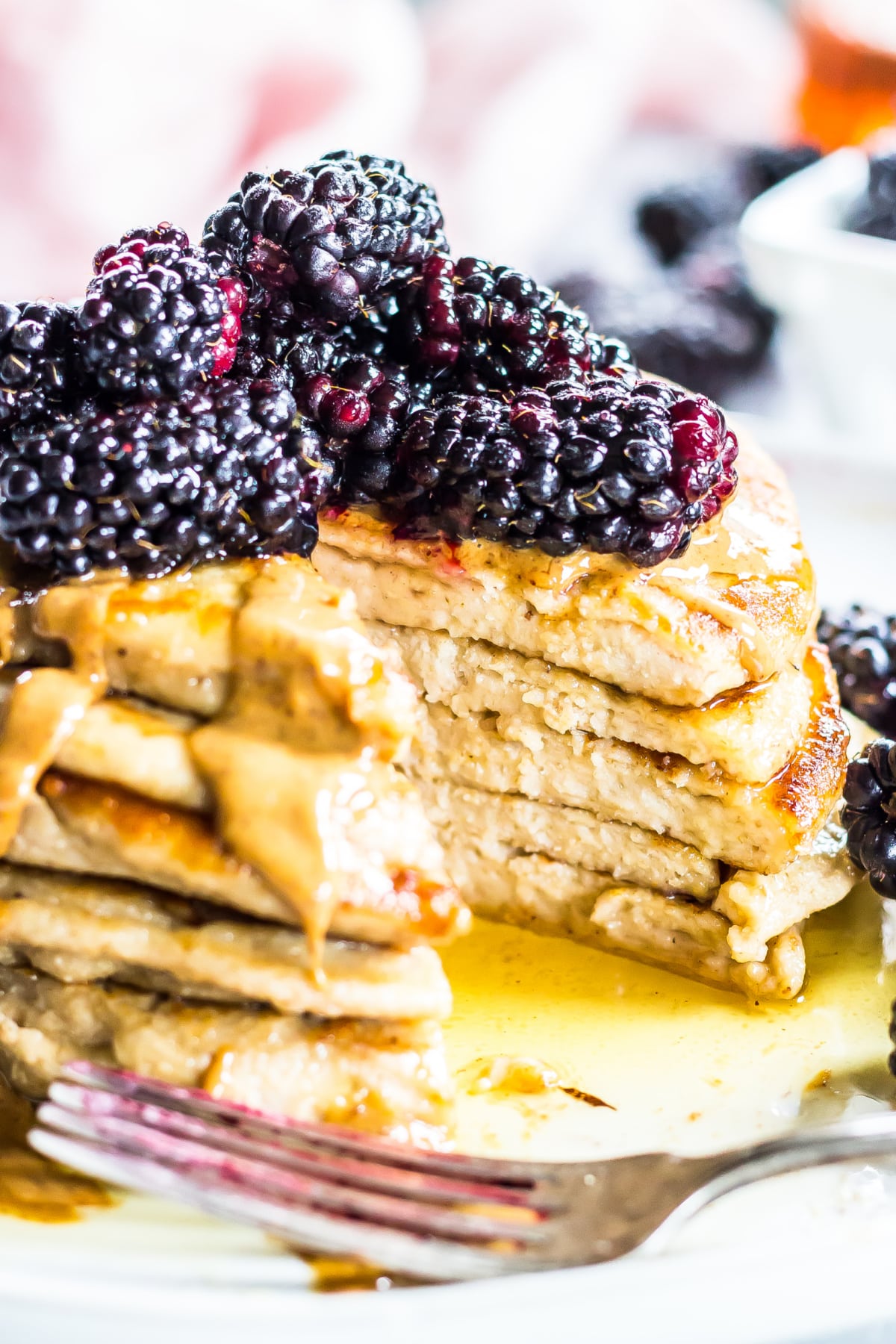 A stack of pancakes topped with peanut butter and blackberries has one bite sliced out, and a fork on the side.