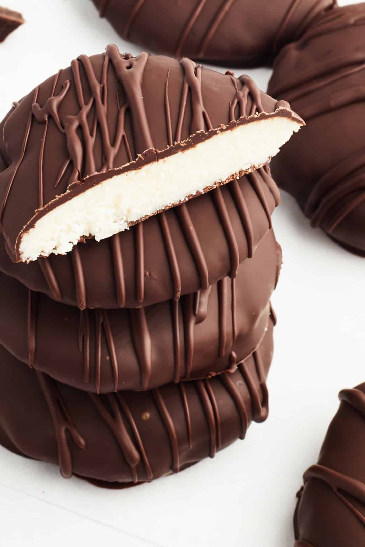 A stack of 4 peppermint patties on a white surface, with more sitting next to the stack. The top one on the stack is sliced open to see the bright white peppermint filling.