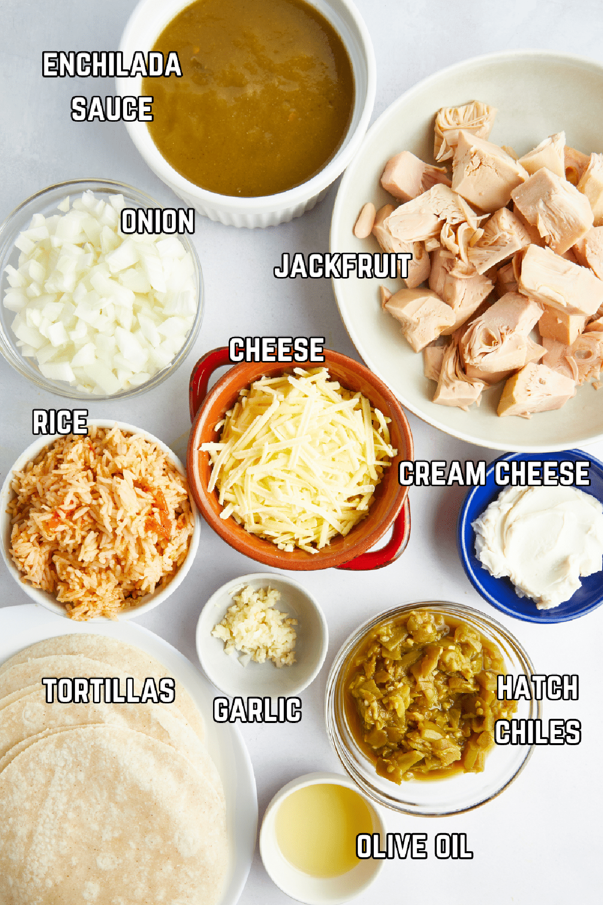 Bowls of ingredients to make Hatch chile enchiladas: sauce, jackfruit, onion, garlic, rice, cheese, cream cheese, tortillas, Hatch chiles, and spices.