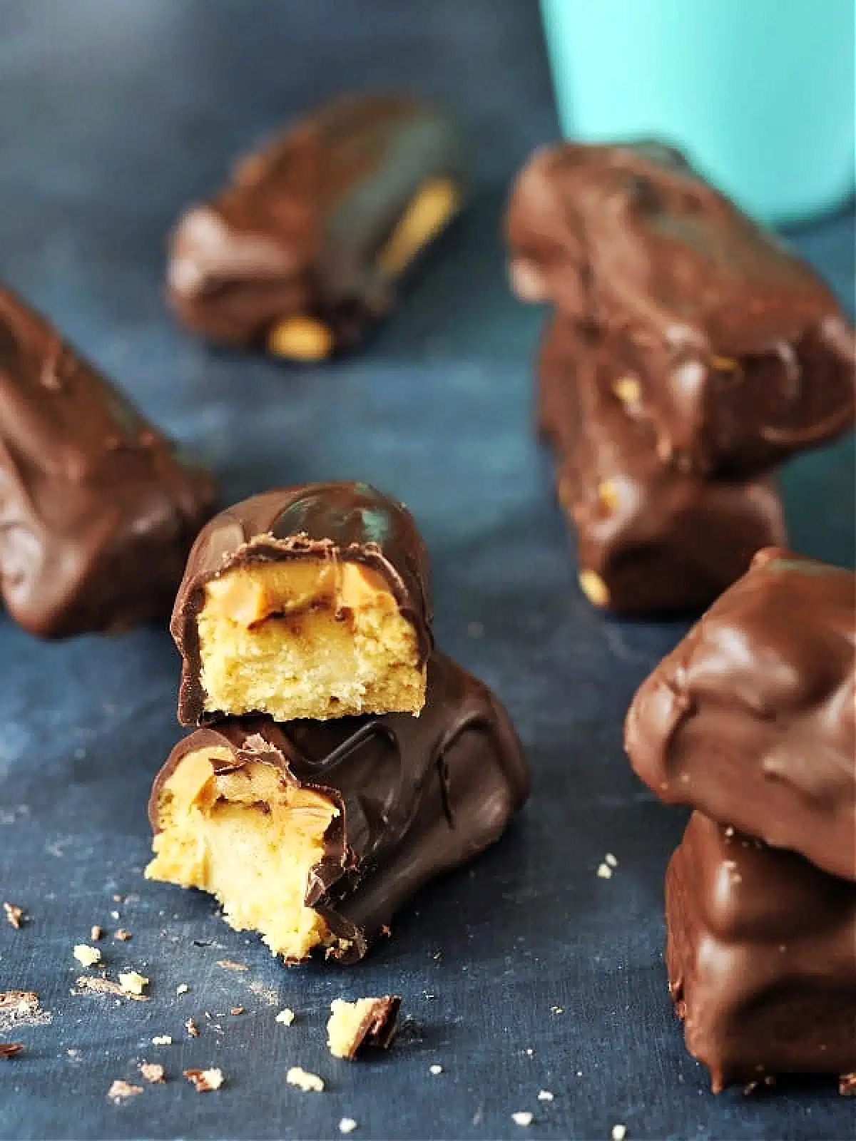 A homemade peanut butter Twix bar broken in half to see the peanut butter and cookie inside. Several chocolate covered bars sit in background.